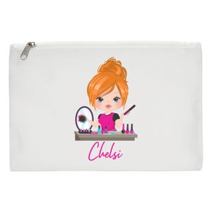 May include: White canvas makeup bag featuring a cartoon illustration of a girl with red hair applying makeup. The girl is holding a makeup brush and looking in a mirror. The bag has the name "Chelsi" printed on it in pink.