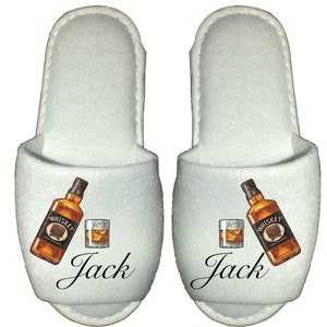 May include: White terry cloth slippers with a graphic of a bottle of whiskey and a glass of whiskey. The slippers have the name "Jack" printed on them.