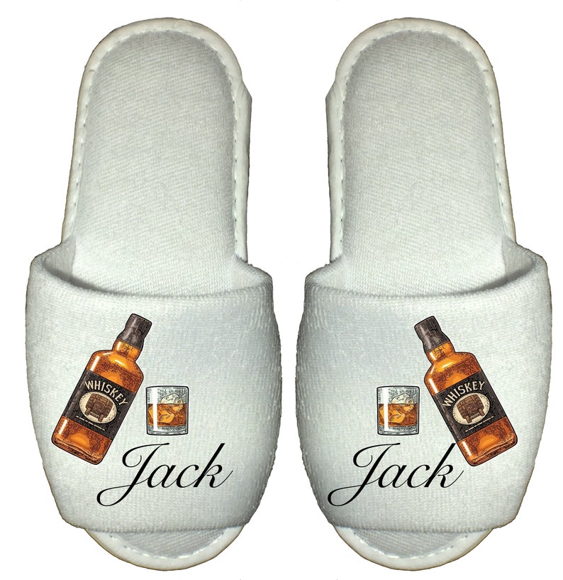 May include: White terry cloth slippers with a graphic of a bottle of whiskey and a glass of whiskey. The slippers have the name "Jack" printed on them.