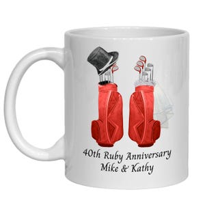 May include: A white ceramic mug featuring a graphic of two red golf bags. One bag has a black top hat on top, and the other has a white veil. Below the bags, the text reads 40th Ruby Anniversary Mike & Kathy in black script.