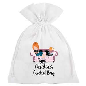 May include: White cotton drawstring bag with a pink couch, a girl crocheting, and two cats. The text "Christine's Crochet Bag" is printed on the bag.