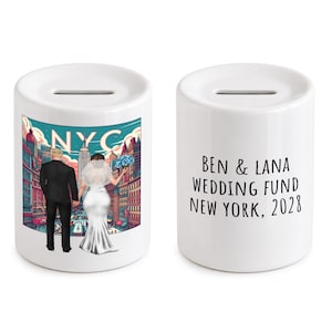 May include: Two white ceramic money boxes with a coin slot on top. One side features a colorful illustration of a couple in wedding attire in New York City with the text NYC. The other side displays the black text BEN & LANA WEDDING FUND NEW YORK, 2028.