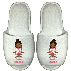 May include: White spa slippers with a cartoon illustration of a girl with brown skin and hair, wearing a pink robe and sitting in a foot bath. The slippers have the name "Brooke" printed on them.