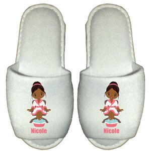 May include: White spa slippers with a cartoon illustration of a woman in a pink robe getting a pedicure. The slippers are personalized with the name "Nicole".