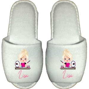 May include: White terry cloth slippers with a pink and white cartoon illustration of a girl doing her makeup. The slippers have the name "Lisa" embroidered on them in pink.