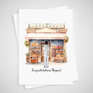 May include: A greeting card featuring a watercolour illustration of a bakery storefront with a person in white clothing standing in front. The shop has a striped awning, shelves of pastries, and hanging plants. The text reads, Congratulations Megan!
