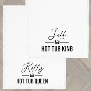 Könnte beinhalten: Zwei weiße, rechteckige Handtücher mit dekorativem Rand. Auf einem Handtuch steht der Name "Jeff" über dem Text "HOT TUB KING". Auf dem anderen Handtuch steht der Name "Kelly" über dem Text "HOT TUB QUEEN".