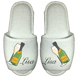 May include: A pair of white slippers with a champagne bottle and glass design. The slippers have the name "Lisa" printed on them.