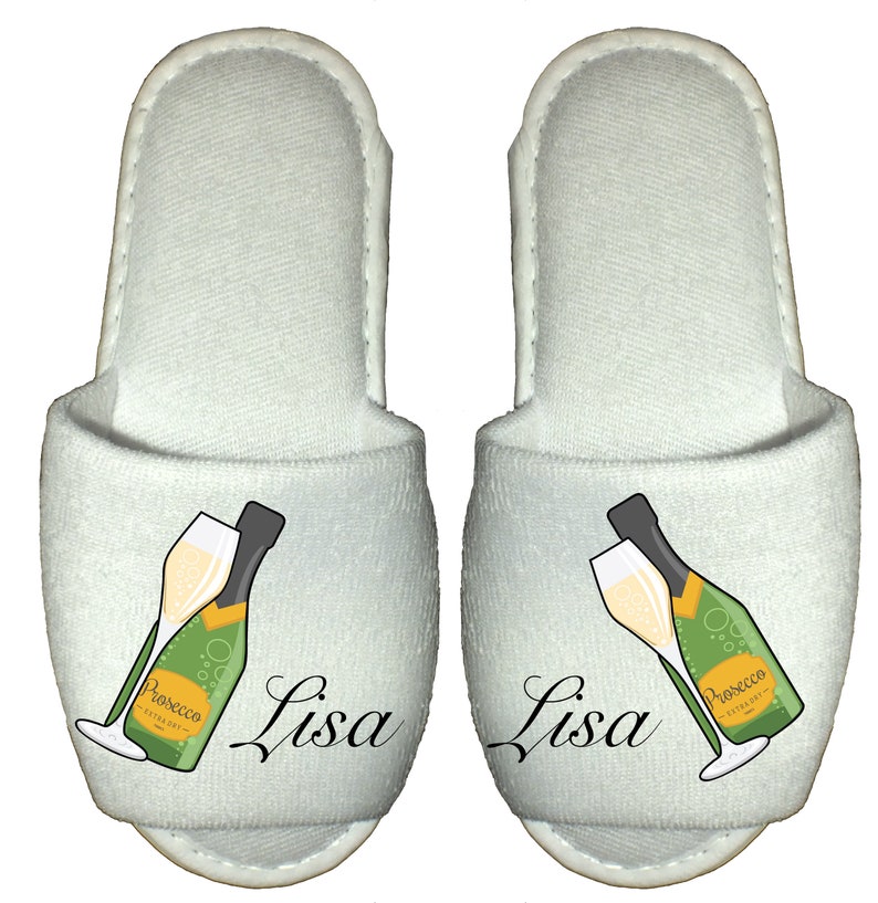 May include: A pair of white slippers with a champagne bottle and glass design. The slippers have the name "Lisa" printed on them.
