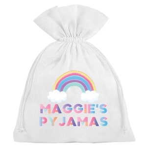 Könnte beinhalten: Ein weißer Kordelzugbeutel mit einem Regenbogen und dem Text "Maggie's Pyjamas" in bunten Buchstaben.