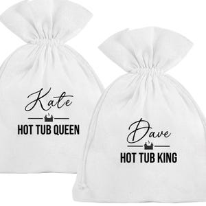 Könnte beinhalten: Zwei weiße Kordelzugbeutel mit schwarzem Text. Auf einem Beutel steht "Kate" über "HOT TUB QUEEN". Auf dem anderen steht "Dave" über "HOT TUB KING". Beide haben eine kleine Grafik eines Whirlpools.