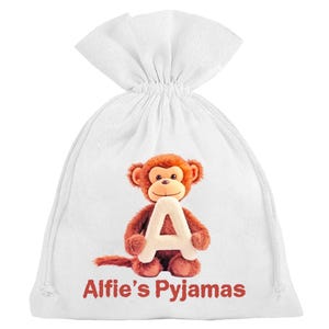 May include: White drawstring bag with a brown monkey holding a white letter 'A'. The text 'Alfie's Pyjamas' is printed in red. The bag is designed for storing pyjamas, a practical and cute gift.