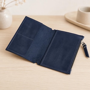 May include: A navy blue leather wallet featuring a bi-fold design with an open interior. The left side includes two card slots, while the right side features a zippered compartment with a matching leather pull tab and visible tonal stitching.