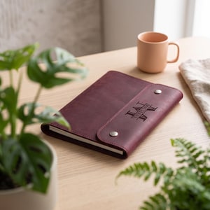 May include: A deep burgundy leather notebook cover featuring a flap closure secured with two silver-toned metal snaps. The front flap is engraved with the name MICHAEL and the initials M.V.I. in a clean, centred, and capitalised font style.