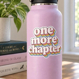 May include: A light purple water bottle with a black lid featuring a sticker that says one more chapter in white letters with a rainbow-colored drop shadow effect. The text is stacked in three lines with a wavy, retro-inspired font style.