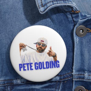 May include: A round white pinback button featuring a graphic of a person wearing a white cap and sunglasses with the text Hotty Toddy, holding a silver chain with an M pendant, and pointing forward. The text PETE GOLDING is printed in blue below.