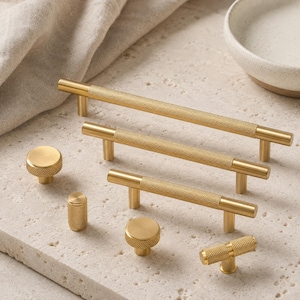 May include: A collection of brushed gold cabinet hardware including three long bar pulls with knurled centre textures, two round knobs with knurled edges, one cylindrical knob with a knurled surface, and one small T-shaped pull with a knurled texture.