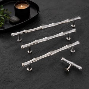 May include: A set of four silver-toned metal cabinet pulls and a matching knob, each featuring a segmented bamboo-inspired design with a polished, reflective finish. The hardware includes three long bar handles of varying lengths and one small knob.