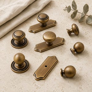 May include: A collection of antique brass cabinet hardware including three round knobs with rope-textured circular backplates, two knobs mounted on rectangular plates with scalloped edges, and three simple spherical knobs in various sizes.