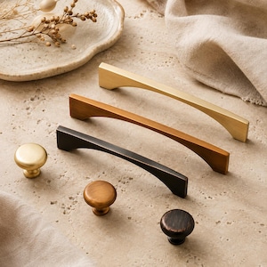 Può includere: Una collezione di ferramenta per mobili che include tre maniglie per cassetti in metallo arcuato e tre pomelli rotondi. Il set presenta una varietà di finiture, tra cui oro spazzolato, ottone antico e nero opaco, disposti in formazione diagonale.