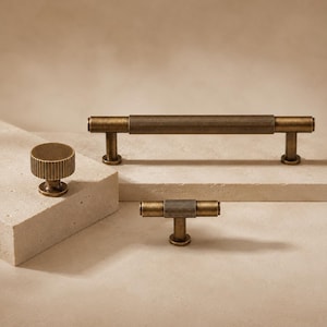 May include: A set of three antique brass cabinet hardware pieces including one long bar pull, one T-shaped knob, and one round knob. Each piece features a textured, ribbed surface design with a consistent metallic finish and cylindrical shapes.
