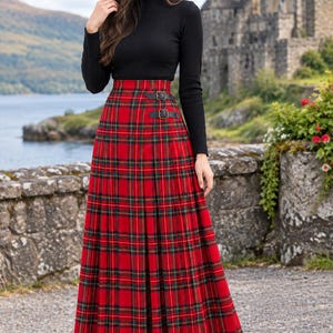 Peut inclure: Une jupe longue rouge à motif tartan avec des lignes vertes et noires, une taille haute et deux lanières latérales en similicuir noir avec des boucles métalliques. La jupe est portée avec un haut noir à manches longues et col montant côtelé.