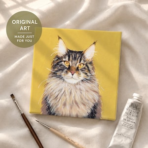 May include: A square canvas painting of a brown and black tabby cat with long fur and amber eyes set against a solid mustard yellow background. The painting is accompanied by two wooden paintbrushes and a tube of Winsor & Newton oil paint.