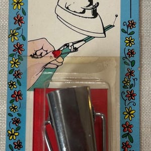 May include: A silver metal bias tape maker on a blue cardboard backing with a floral border. The packaging text reads BIAS Tape Maker, MAKES 1/2" TAPE FOR SEWING AND CRAFT PROJECTS, and No. 3. An illustration shows the tool being used with an iron.