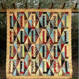 May include: A rectangular quilt featuring a geometric pattern of triangles and vertical strips in various colors including red, blue, brown, black, and cream. The quilt is framed by a solid tan border and displays a mix of solid and patterned fabrics.