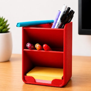 May include: A bright red desk organizer with three tiered compartments. The top section holds a light blue marker, a purple pen, a white pen, and three black pens. The middle section holds a pink, yellow, and red marker. A yellow notepad sits below.