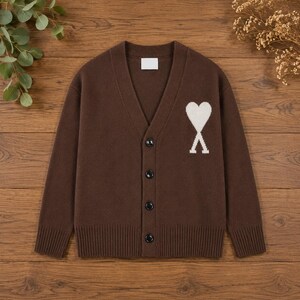 May include: A dark brown V-neck cardigan featuring a white heart-shaped logo on the left chest. The knit garment has long sleeves, a ribbed hem and cuffs, and a front button closure with four dark buttons. A white rectangular label is at the neck.