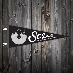 May include: Black pennant flag with a white silhouette of the St. Louis skyline and a record player. The text "St. Louis" is written in a white cursive font with the words "JAZZ, BLUES, ROCK 'N' ROLL & SOUL" below.