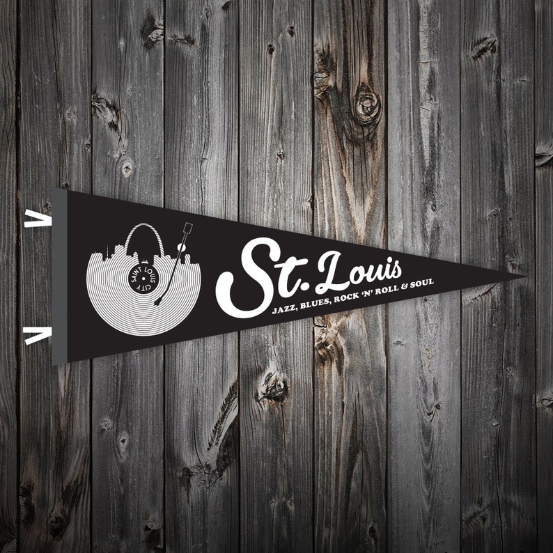 May include: Black pennant flag with a white silhouette of the St. Louis skyline and a record player. The text "St. Louis" is written in a white cursive font with the words "JAZZ, BLUES, ROCK 'N' ROLL & SOUL" below.