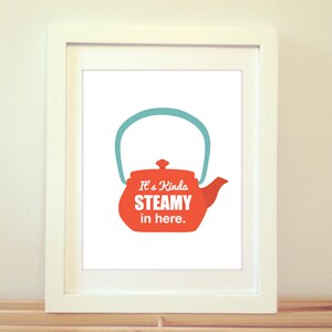 May include: A white framed print with a red teapot with a teal lid and handle. The text on the print reads "It's Kinda STEAMY in here."
