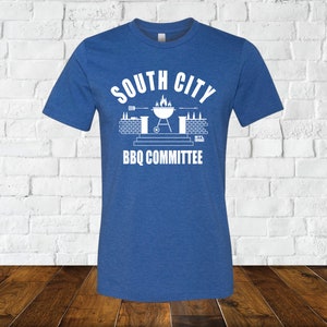 May include: A royal blue t-shirt with a white graphic design of a grill, flames, and the text "South City BBQ Committee".