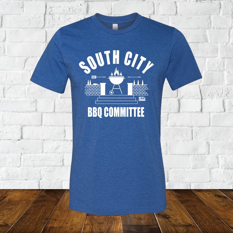 May include: A royal blue t-shirt with a white graphic design of a grill, flames, and the text "South City BBQ Committee".