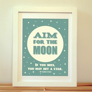 May include: A teal blue framed print with a white circle in the center. The circle has the text "AIM FOR THE MOON" in white with a black outline. Below the circle is the text "IF YOU MISS, YOU MAY HIT A STAR." in white with a black outline. The text "W. CLEMENT STONE" is below the quote in a smaller font. The background is filled with white stars.