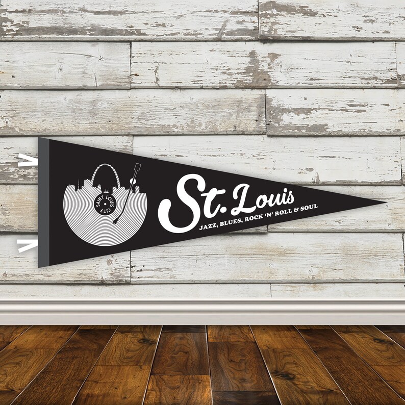 May include: Black pennant flag with a white silhouette of the St. Louis skyline and a record player. The text "St. Louis" is written in a white cursive font with the words "Jazz, Blues, Rock 'n' Roll & Soul" underneath.