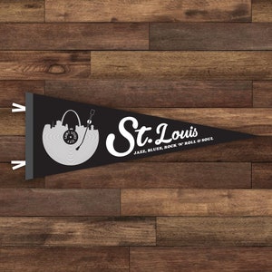May include: Black pennant flag with a white silhouette of the St. Louis skyline and a record player. The text "St. Louis" is written in a white cursive font with the words "JAZZ, BLUES, ROCK 'N' ROLL & SOUL" below.