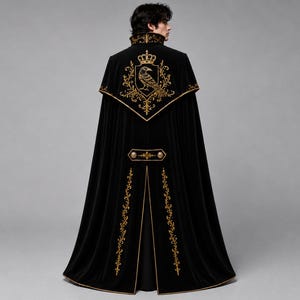 May include: A floor-length black velvet cape featuring gold embroidery. The back displays a large crest with a crown and a raven. Additional gold floral embroidery accents the collar, the horizontal back panel, and the vertical hem edges.