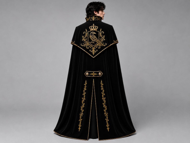May include: A floor-length black velvet cape featuring gold embroidery. The back displays a large crest with a crown and a raven. Additional gold floral embroidery accents the collar, the horizontal back panel, and the vertical hem edges.