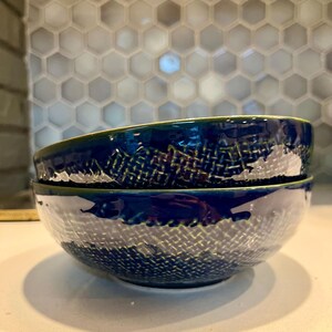 May include: Two stacked ceramic bowls featuring a deep navy blue glaze with a textured, woven-like pattern visible through the finish. The bowls have a smooth, glossy surface and a dark green rim, showcasing a rounded shape and a sturdy base.