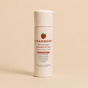 Peut inclure: Un flacon pompe cylindrique blanc de crème resurfaçante Strawberry Ultra-Strength Strawberry Skin. L'étiquette présente une petite icône de fraise et liste les ingrédients : acide glycolique 6%, acide salicylique 1%, niacinamide 2%, acide lactique 0,5%, urée 2%. Contenu 118 ml.