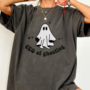 May include: A charcoal gray short-sleeve t-shirt featuring a white ghost graphic centered on the chest. The text "CEO of ghosting" is printed in black below the ghost, accompanied by small black star icons surrounding the central design.