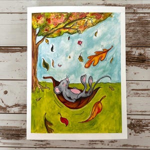 May include: A watercolor illustration of a gray mouse with pink ears and belly resting inside a large brown fallen leaf. The scene features a green grassy field, a tree with autumn foliage, and various colorful leaves floating in a light blue sky.