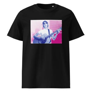 May include: A black short-sleeve t-shirt featuring a rectangular graphic print on the chest. The print displays a person wearing sunglasses and a white t-shirt while playing an acoustic guitar, rendered in a stylized blue and magenta color palette.