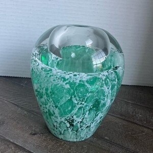May include: A clear glass vase featuring a rounded top section and a wider base with a mottled pattern of vibrant emerald green and opaque white glass. The surface displays a textured, marbled appearance with varying densities of color throughout.