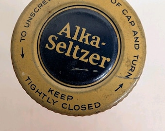 Puede incluir: Una tapa de botella redonda de metal color canela con un centro azul oscuro que presenta el texto Alka-Seltzer en dorado. El borde color canela incluye el texto negro TO UNSCREW-TAP EDGE OF CAP AND TURN y KEEP TIGHTLY CLOSED con flechas.