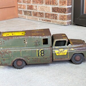 May include: A vintage olive green metal toy utility truck featuring the number 18 on the side and a yellow decal on the door that reads Lumar Utility Service with a telephone icon. The truck shows significant rust and wear across its surface.