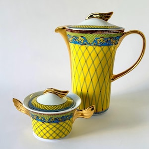 May include: A tall porcelain coffee pot and a matching sugar bowl with lids. Both pieces feature a bright yellow diamond lattice pattern, a blue band with gold scrollwork, and gold-toned handles, spouts, and finials on the white lids.